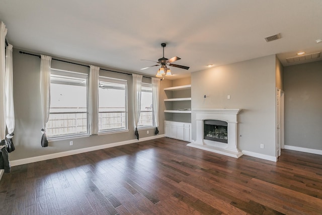 unfurnished living room with visible vents, a fireplace with raised hearth, wood finished floors, baseboards, and ceiling fan