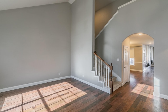 staircase with baseboards, arched walkways, high vaulted ceiling, and wood finished floors