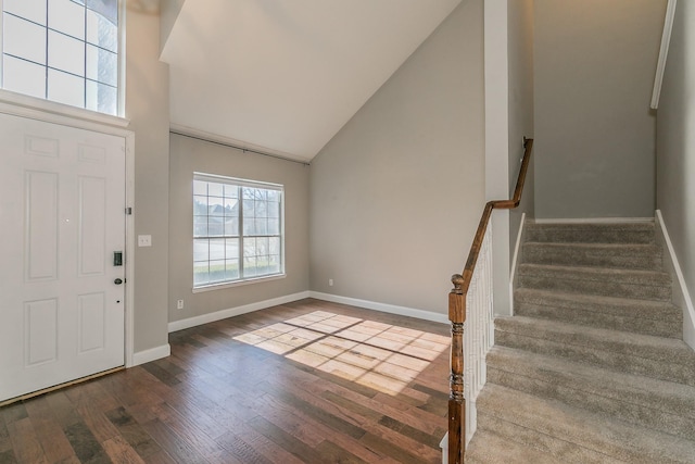 entrance foyer with wood finished floors, stairs, baseboards, and high vaulted ceiling