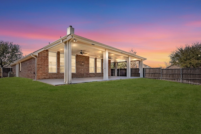 back of property at dusk featuring ceiling fan, a patio, a chimney, brick siding, and cooling unit