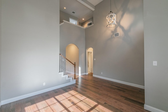 entrance foyer featuring arched walkways, stairway, a towering ceiling, wood finished floors, and a chandelier