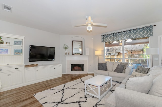 living area with a ceiling fan, baseboards, wood finished floors, visible vents, and a tile fireplace