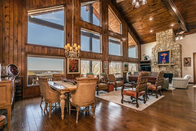 dining space featuring dark wood-style floors, a stone fireplace, ceiling fan with notable chandelier, and wood ceiling