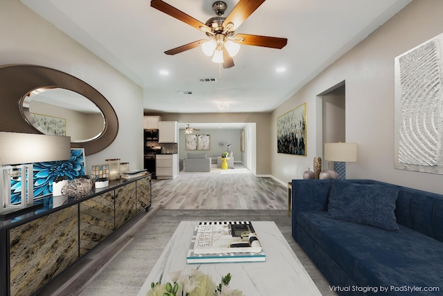 living area featuring a ceiling fan, wood finished floors, visible vents, and baseboards