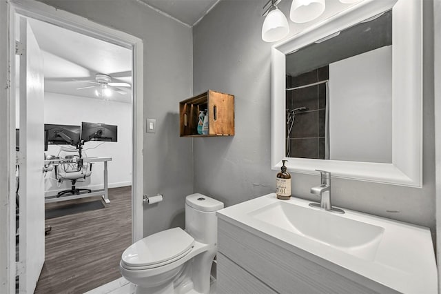 full bathroom with vanity, a ceiling fan, wood finished floors, tiled shower, and toilet