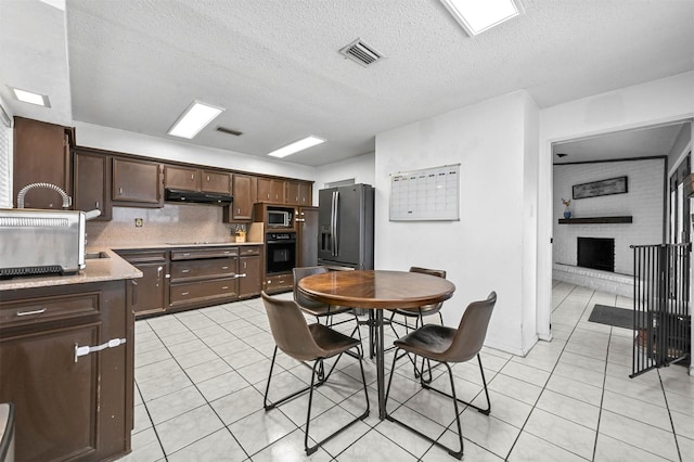 kitchen featuring light tile patterned floors, visible vents, black appliances, dark brown cabinetry, and under cabinet range hood