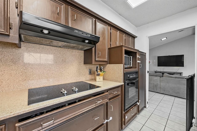 kitchen featuring under cabinet range hood, lofted ceiling, light tile patterned floors, decorative backsplash, and black appliances