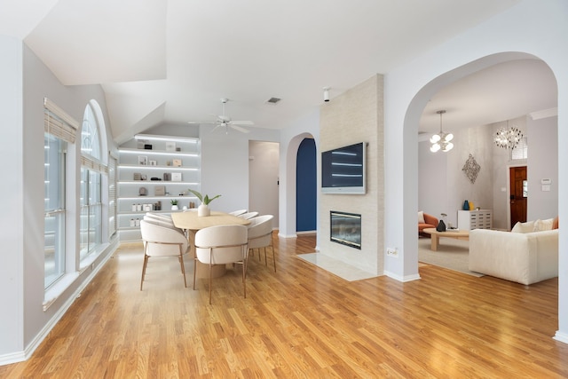 dining room featuring light wood finished floors, ceiling fan with notable chandelier, a fireplace, and arched walkways