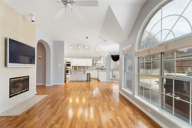 unfurnished living room featuring baseboards, ceiling fan, a fireplace with flush hearth, light wood-style flooring, and arched walkways