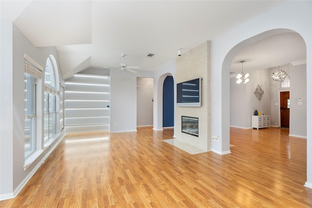 unfurnished living room with light wood-type flooring, baseboards, a fireplace, and ceiling fan with notable chandelier