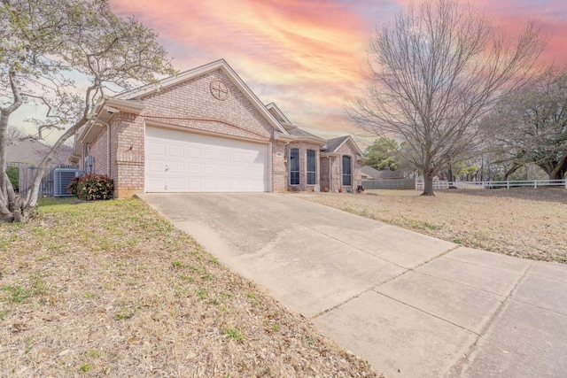 ranch-style home with fence, an attached garage, central AC, concrete driveway, and brick siding