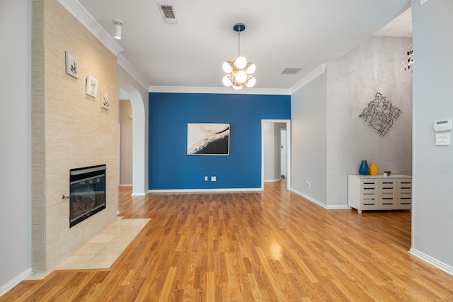 unfurnished living room featuring visible vents, crown molding, a tiled fireplace, light wood-style floors, and arched walkways