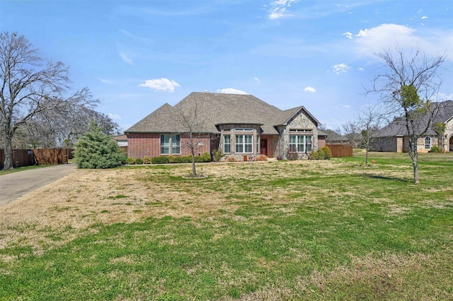 french provincial home with brick siding, a front lawn, and fence