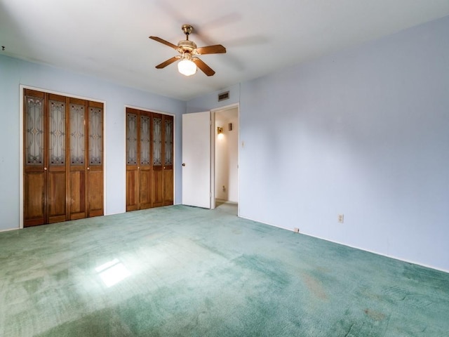 unfurnished bedroom featuring visible vents, two closets, carpet flooring, and a ceiling fan