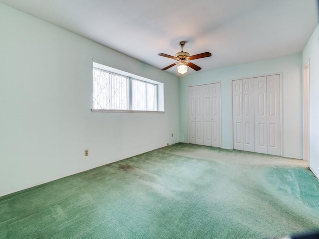 unfurnished bedroom with carpet flooring, a ceiling fan, and two closets