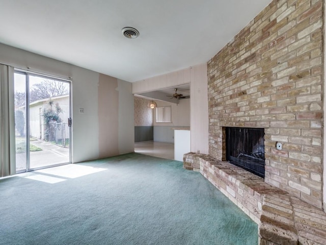 unfurnished living room featuring a brick fireplace, visible vents, carpet floors, and ceiling fan