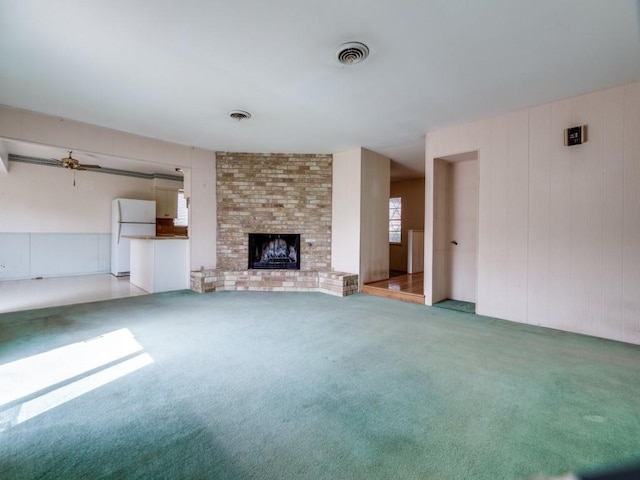 unfurnished living room with a brick fireplace, carpet flooring, a ceiling fan, and visible vents