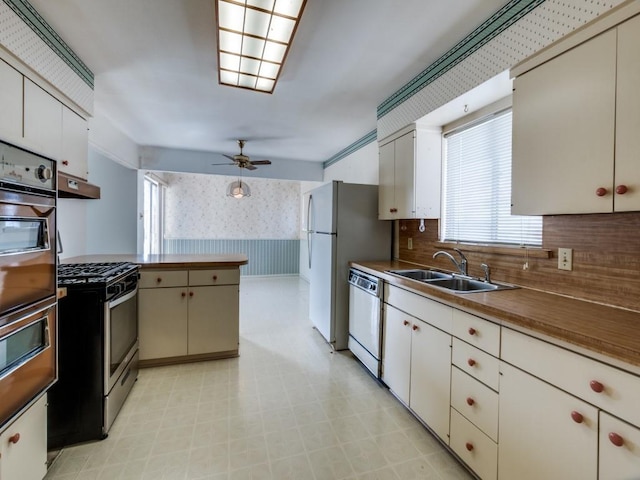 kitchen featuring wall oven, wallpapered walls, gas range, dishwasher, and a sink