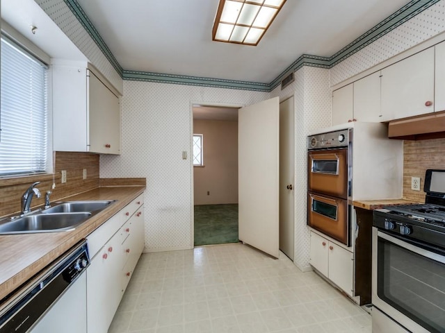 kitchen with multiple ovens, a sink, stainless steel range with gas cooktop, wallpapered walls, and dishwasher