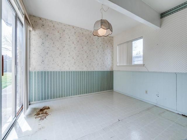 unfurnished room featuring tile patterned floors, a wainscoted wall, beamed ceiling, and wallpapered walls