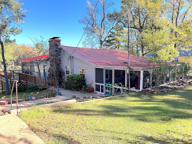 rear view of property with metal roof, a lawn, a chimney, and a sunroom