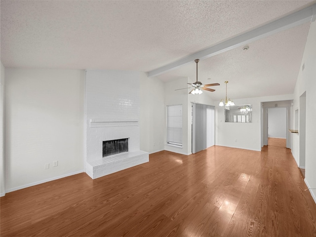 unfurnished living room with a brick fireplace, vaulted ceiling with beams, ceiling fan with notable chandelier, wood finished floors, and a textured ceiling