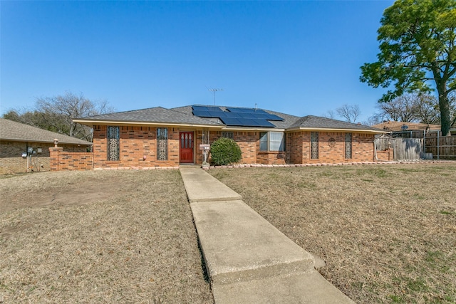 ranch-style house with brick siding, fence, a front yard, roof mounted solar panels, and a gate