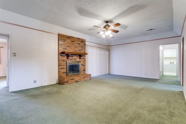 unfurnished living room with a ceiling fan, visible vents, carpet floors, a textured ceiling, and a brick fireplace