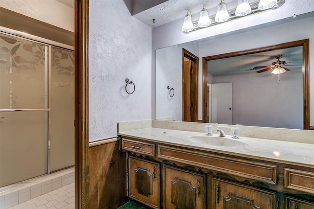 full bath featuring a shower stall, ceiling fan, a wainscoted wall, a textured wall, and vanity