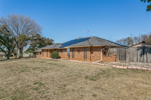 rear view of house with a yard, fence, brick siding, and roof mounted solar panels