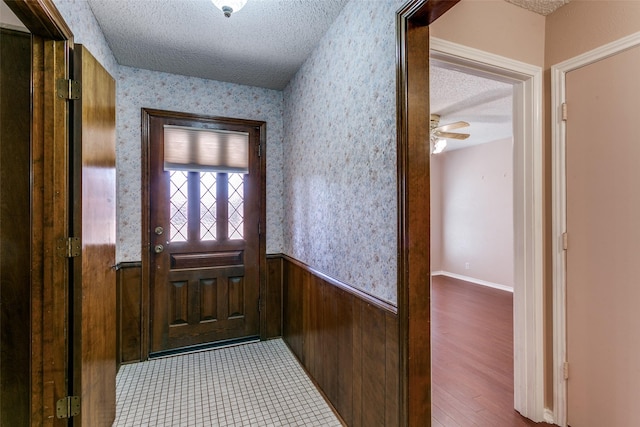 entryway featuring a wainscoted wall, a textured ceiling, and wallpapered walls