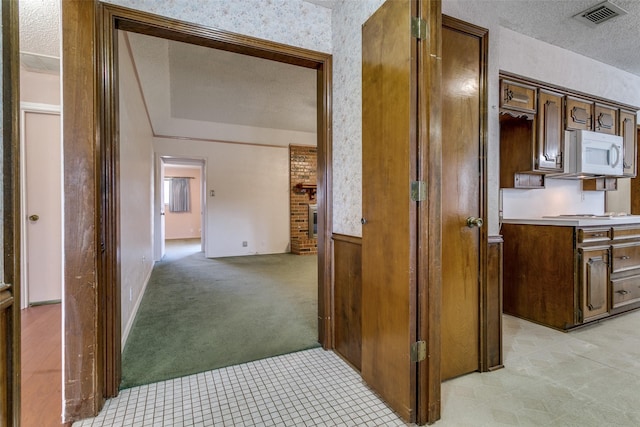 hall with visible vents, light colored carpet, and a textured ceiling