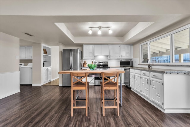 kitchen with independent washer and dryer, a sink, a tray ceiling, appliances with stainless steel finishes, and white cabinets