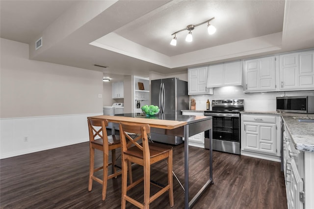 kitchen with a raised ceiling, custom range hood, washing machine and dryer, and appliances with stainless steel finishes