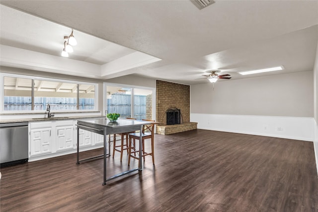 kitchen with a brick fireplace, ceiling fan, dishwasher, dark wood-style floors, and white cabinetry