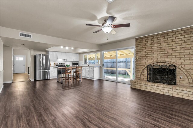 unfurnished living room with visible vents, baseboards, a brick fireplace, ceiling fan, and dark wood-style flooring