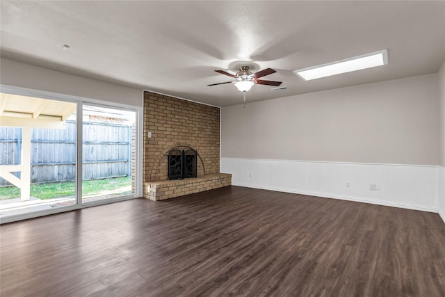 unfurnished living room featuring visible vents, a brick fireplace, dark wood-type flooring, ceiling fan, and a skylight