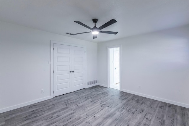 unfurnished bedroom with wood finished floors, visible vents, a closet, and baseboards