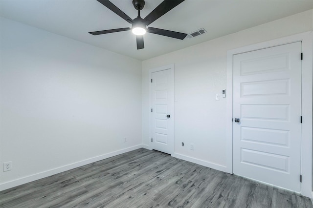 empty room featuring ceiling fan, visible vents, baseboards, and wood finished floors