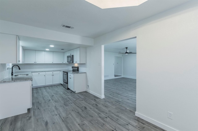 kitchen with light wood-style flooring, a sink, white cabinetry, appliances with stainless steel finishes, and light stone countertops