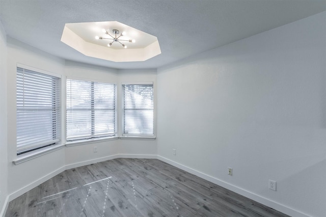 spare room with a notable chandelier, a raised ceiling, baseboards, and wood finished floors