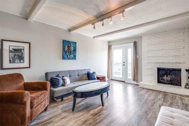 living room with beamed ceiling, a fireplace, french doors, wood finished floors, and a textured ceiling