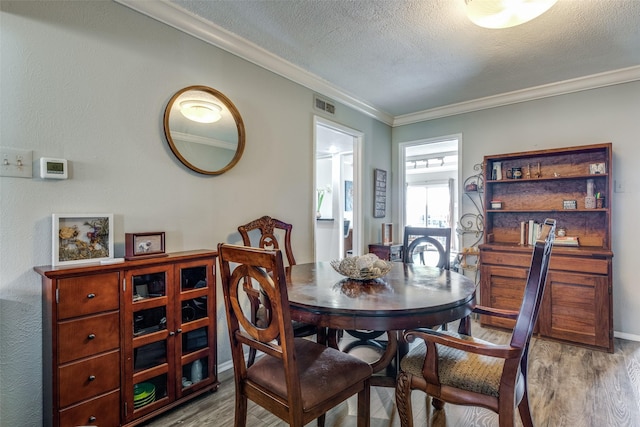 dining space featuring visible vents, a textured ceiling, wood finished floors, and ornamental molding