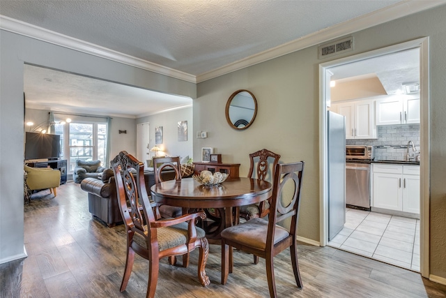 dining room featuring visible vents, ornamental molding, a textured ceiling, light wood-style floors, and a toaster