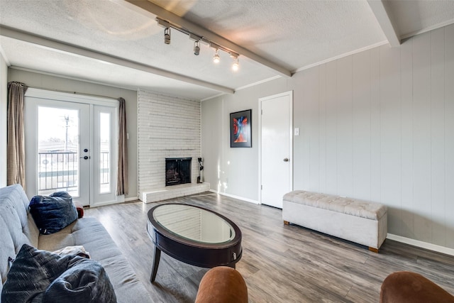 living area with wood finished floors, baseboards, beam ceiling, a fireplace, and a textured ceiling