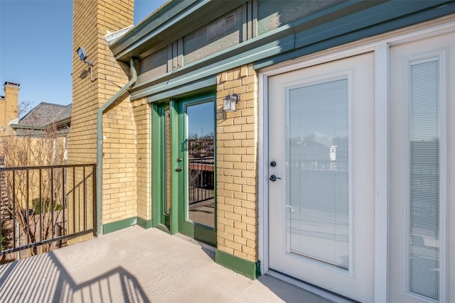 view of exterior entry with a balcony, brick siding, and a chimney