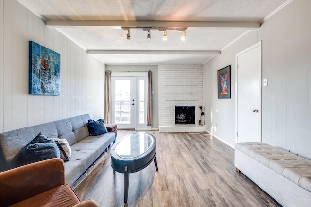 living room with beamed ceiling, a brick fireplace, a textured ceiling, and wood finished floors