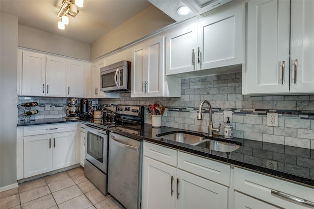 kitchen featuring light tile patterned flooring, a sink, decorative backsplash, white cabinets, and appliances with stainless steel finishes