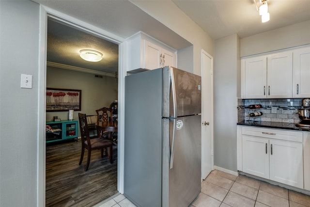 kitchen featuring light tile patterned flooring, freestanding refrigerator, ornamental molding, white cabinetry, and backsplash