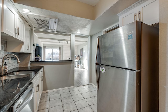 kitchen featuring light tile patterned floors, a sink, stainless steel appliances, white cabinets, and backsplash